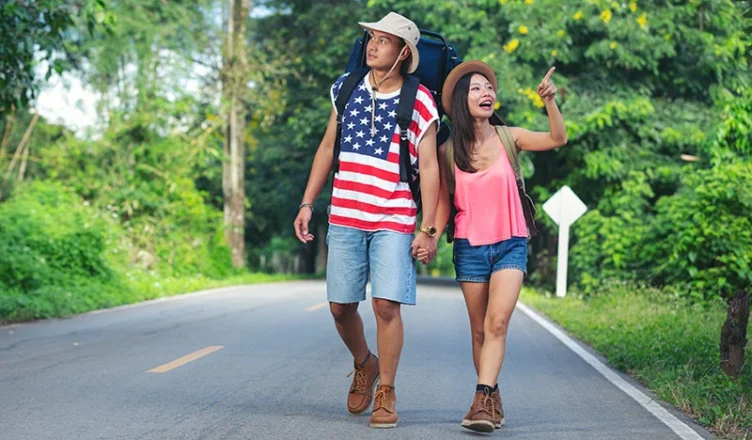 Two travelers walking down a countryside road in the USA during July.